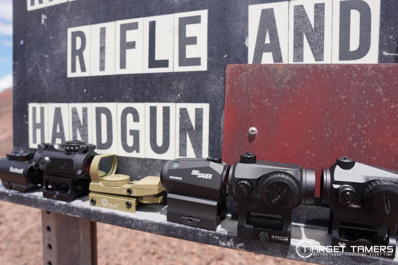 Assorted red dot sights lined up at shooting range